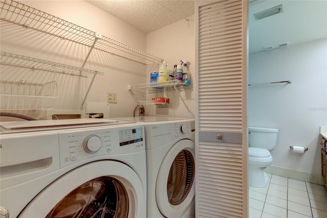 laundry room featuring washing machine and clothes dryer, light tile patterned floors, and a textured ceiling