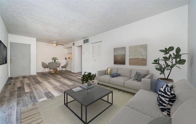 living room with a textured ceiling, ceiling fan, and hardwood / wood-style flooring