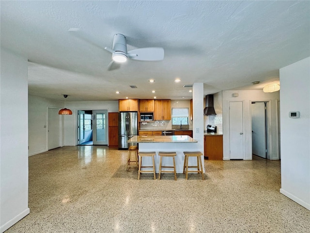 kitchen with wall chimney range hood, sink, appliances with stainless steel finishes, tasteful backsplash, and a kitchen bar