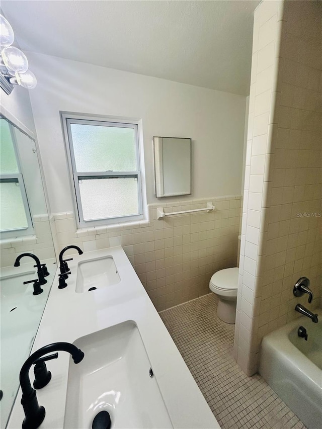 full bathroom featuring vanity, tile patterned flooring, tiled shower / bath combo, toilet, and tile walls