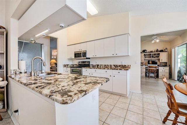 kitchen with light stone countertops, appliances with stainless steel finishes, white cabinetry, sink, and kitchen peninsula