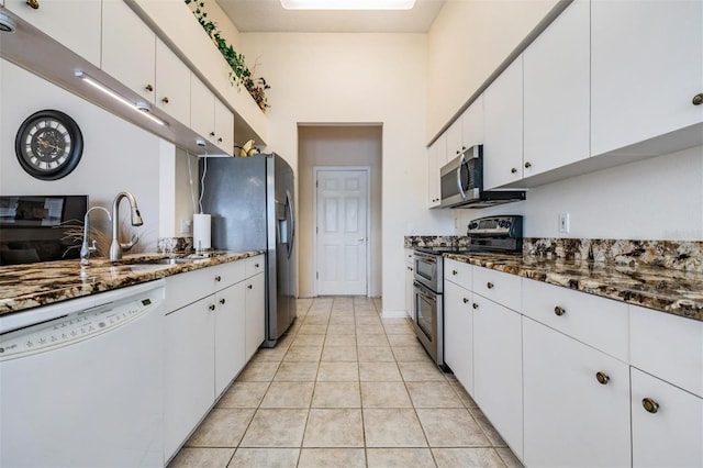 kitchen with white cabinetry, stainless steel appliances, dark stone countertops, sink, and light tile patterned flooring