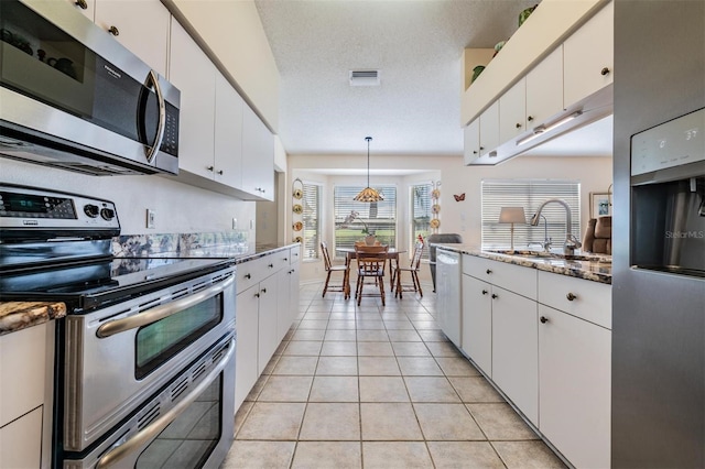 kitchen with a textured ceiling, decorative light fixtures, white cabinetry, stainless steel appliances, and sink