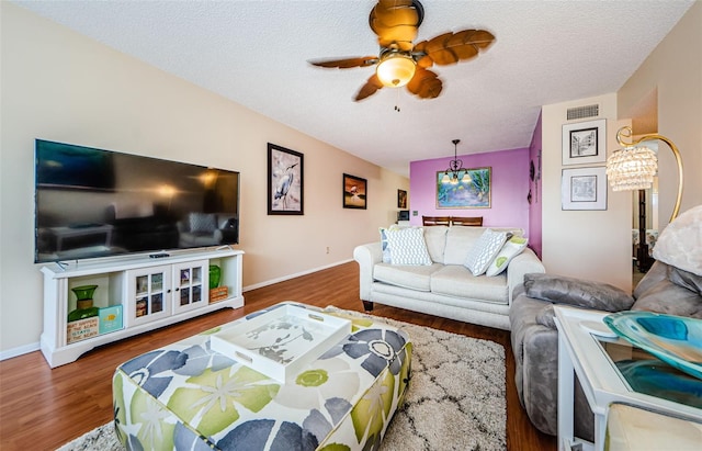 living room with ceiling fan with notable chandelier, wood-type flooring, and a textured ceiling