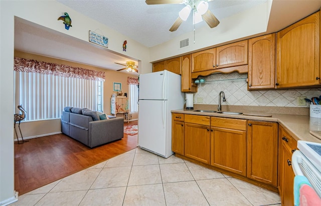 kitchen featuring decorative backsplash, stove, sink, light tile patterned floors, and white refrigerator