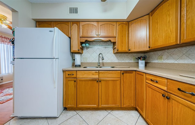 kitchen featuring light tile patterned floors, white refrigerator, tasteful backsplash, and sink