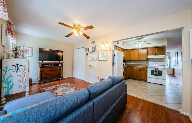 living room with a textured ceiling, light hardwood / wood-style flooring, and ceiling fan