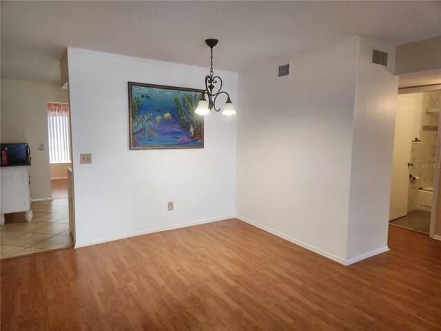 unfurnished dining area featuring a chandelier, a textured ceiling, and hardwood / wood-style flooring