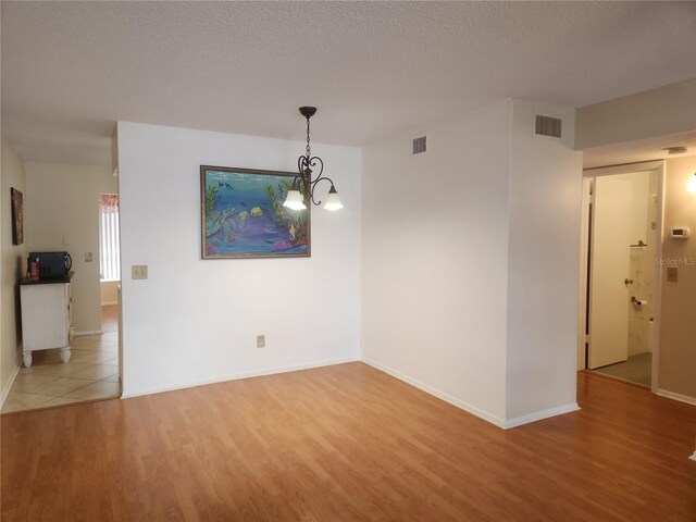 spare room featuring hardwood / wood-style floors, a textured ceiling, and a notable chandelier