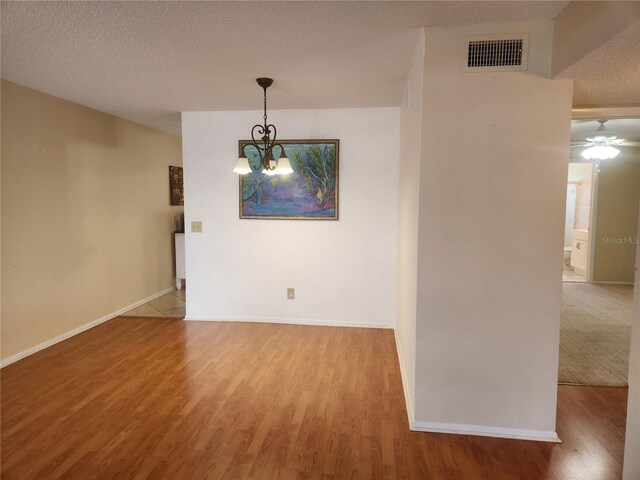 empty room featuring hardwood / wood-style floors, ceiling fan with notable chandelier, and a textured ceiling