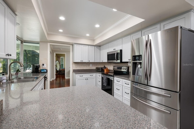 kitchen featuring white cabinets, light stone counters, appliances with stainless steel finishes, and a tray ceiling