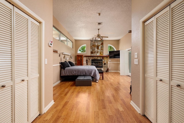 bedroom with a textured ceiling, light hardwood / wood-style floors, a fireplace, and multiple closets