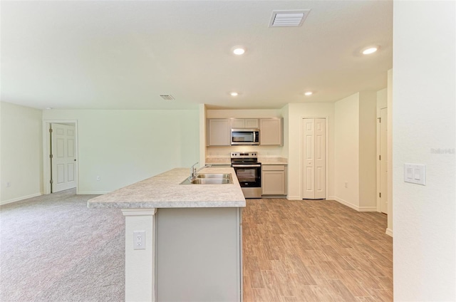 kitchen with appliances with stainless steel finishes, sink, gray cabinets, light hardwood / wood-style floors, and an island with sink