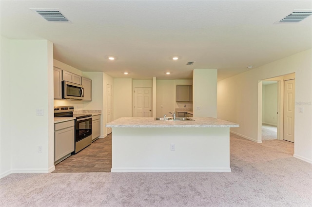 kitchen with an island with sink, light colored carpet, and appliances with stainless steel finishes