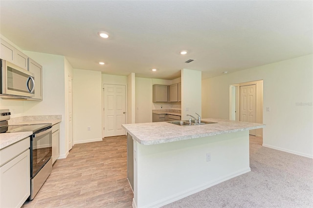 kitchen featuring a kitchen island with sink, sink, light wood-type flooring, and appliances with stainless steel finishes