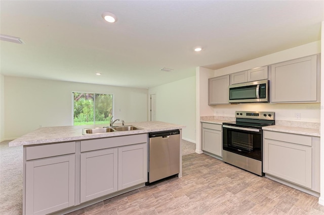 kitchen featuring a center island with sink, sink, gray cabinets, light wood-type flooring, and stainless steel appliances