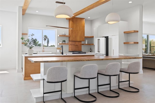 kitchen with a breakfast bar, high end white refrigerator, sink, white cabinets, and hanging light fixtures