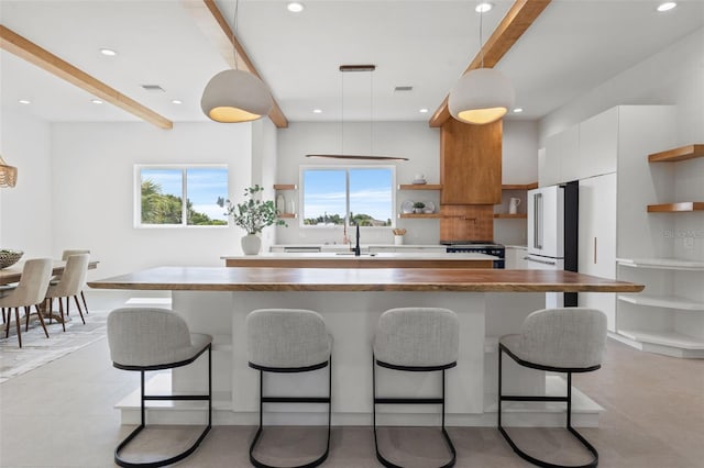 kitchen with pendant lighting, sink, high quality fridge, white cabinetry, and range with gas cooktop