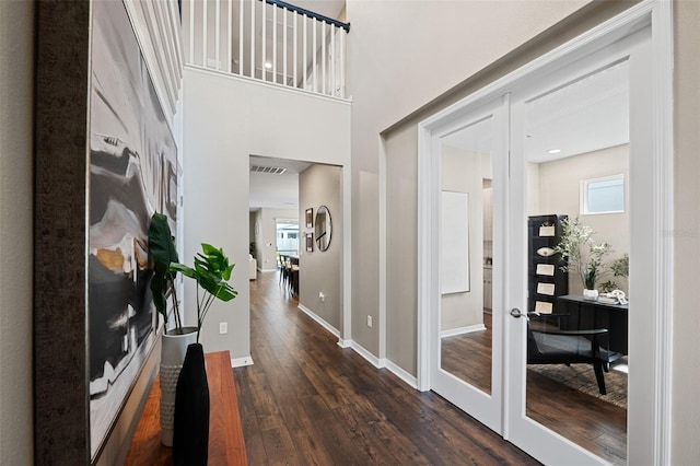 corridor with dark wood-type flooring, a towering ceiling, and french doors