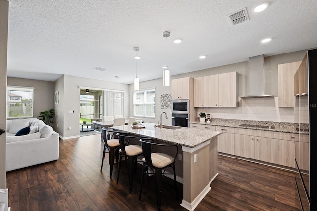 kitchen with stainless steel appliances, wall chimney range hood, an island with sink, pendant lighting, and a breakfast bar area