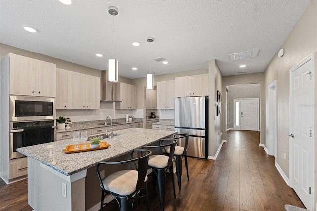 kitchen with dark wood-type flooring, a center island with sink, hanging light fixtures, light stone countertops, and stainless steel appliances