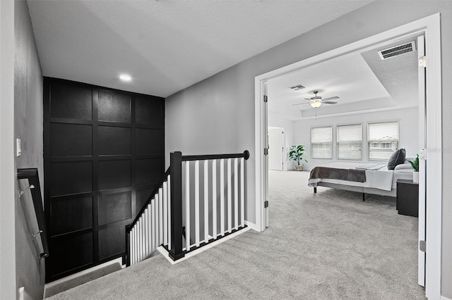 hall featuring a textured ceiling, light carpet, and a tray ceiling