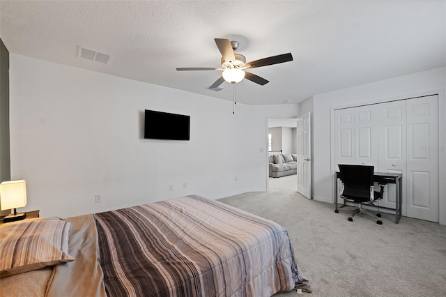 bedroom with ceiling fan, light colored carpet, a textured ceiling, and a closet