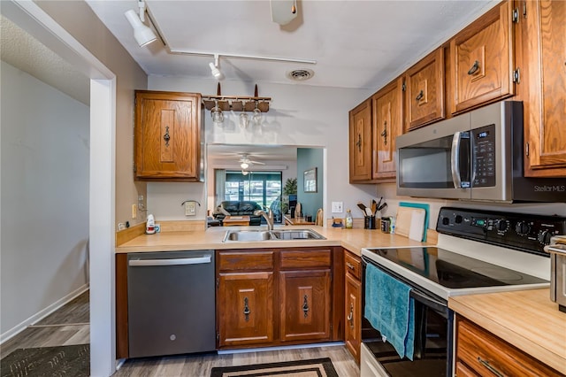 kitchen featuring sink, rail lighting, ceiling fan, appliances with stainless steel finishes, and light hardwood / wood-style floors