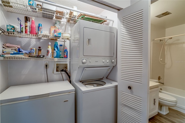 laundry area with hardwood / wood-style flooring and stacked washer / dryer