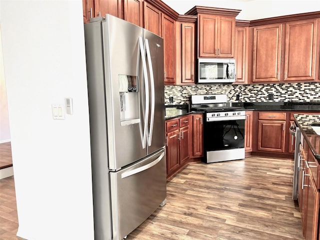 kitchen with appliances with stainless steel finishes, dark stone counters, wood-type flooring, and backsplash