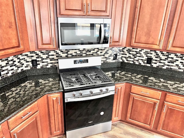 kitchen with backsplash, appliances with stainless steel finishes, light hardwood / wood-style floors, and dark stone counters