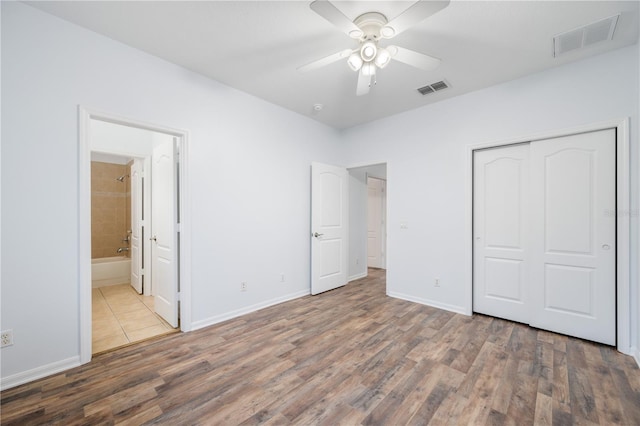 unfurnished bedroom featuring hardwood / wood-style floors, ensuite bath, a closet, and ceiling fan