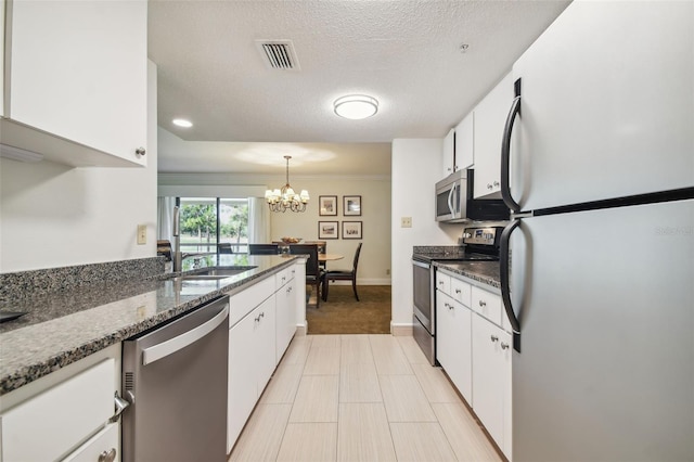 kitchen featuring dark stone countertops, a textured ceiling, appliances with stainless steel finishes, white cabinetry, and a chandelier