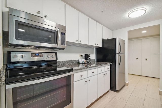 kitchen with a textured ceiling, stainless steel appliances, white cabinetry, and dark stone countertops