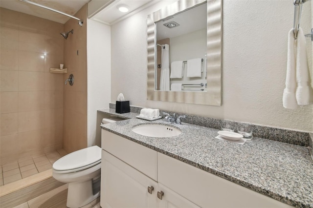 bathroom featuring tiled shower, hardwood / wood-style flooring, vanity, and toilet