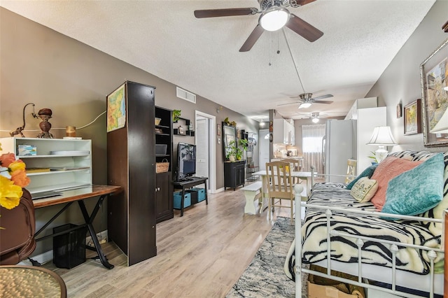 bedroom with light wood-type flooring, white fridge, ceiling fan, and a textured ceiling