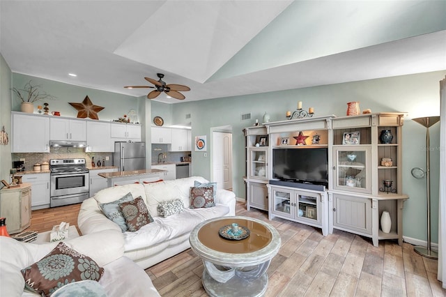 living room featuring ceiling fan, sink, light hardwood / wood-style flooring, and vaulted ceiling