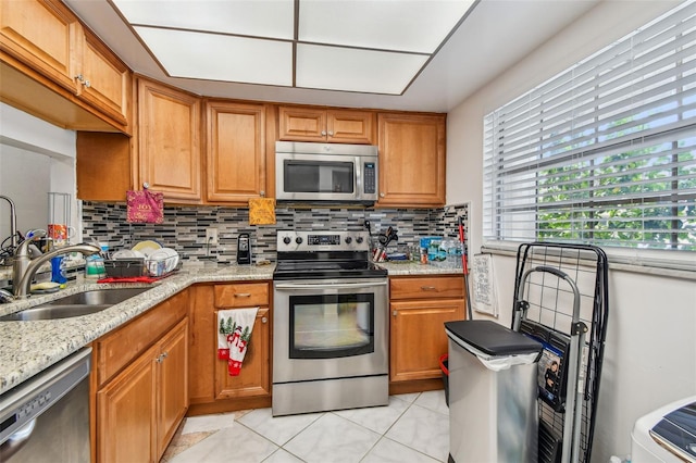 kitchen with tasteful backsplash, stainless steel appliances, light tile flooring, light stone counters, and sink