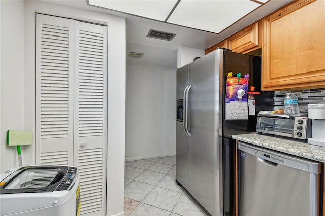 kitchen with appliances with stainless steel finishes, washer / dryer, light stone counters, tasteful backsplash, and light tile floors