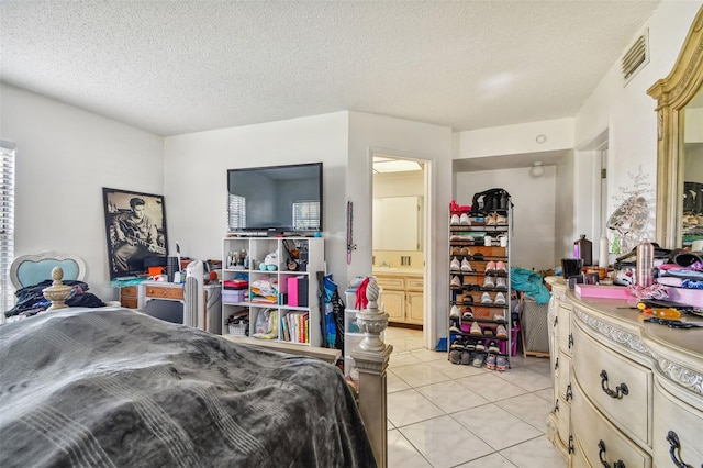 bedroom with ensuite bathroom, a textured ceiling, and light tile flooring