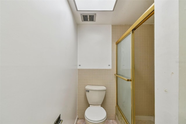 bathroom featuring tile flooring, tile walls, toilet, and a shower with door