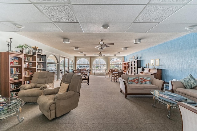 living room featuring ceiling fan, carpet floors, and a drop ceiling