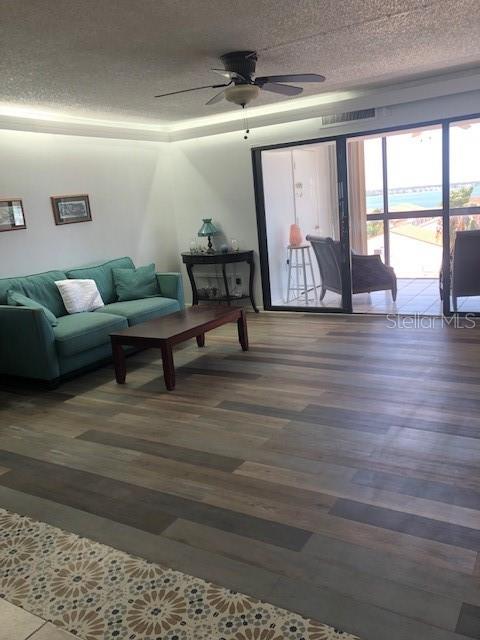 living room featuring a textured ceiling, dark wood-type flooring, and ceiling fan