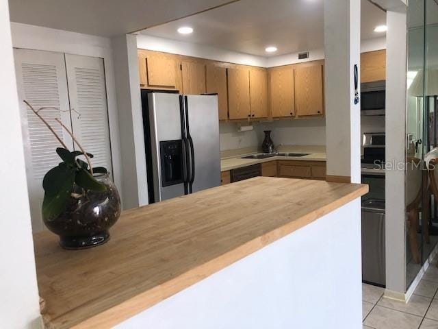 kitchen with light tile patterned floors, appliances with stainless steel finishes, kitchen peninsula, sink, and wooden counters