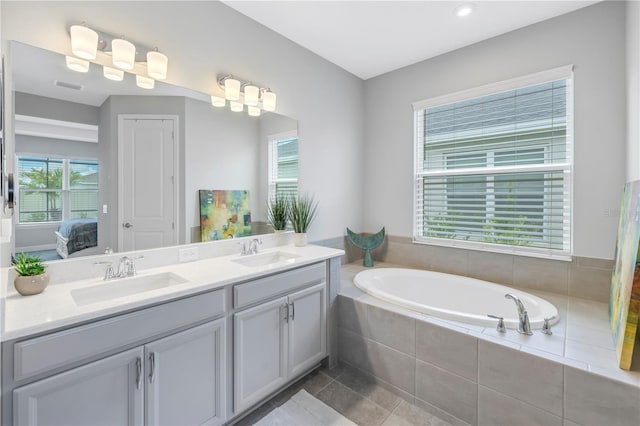 bathroom featuring tiled bath, vanity, and tile patterned flooring