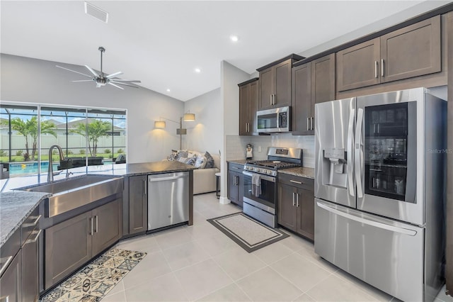 kitchen with dark brown cabinets, appliances with stainless steel finishes, sink, decorative backsplash, and lofted ceiling