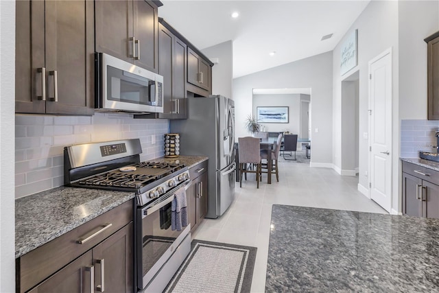 kitchen featuring stainless steel appliances, tasteful backsplash, dark stone countertops, vaulted ceiling, and dark brown cabinets