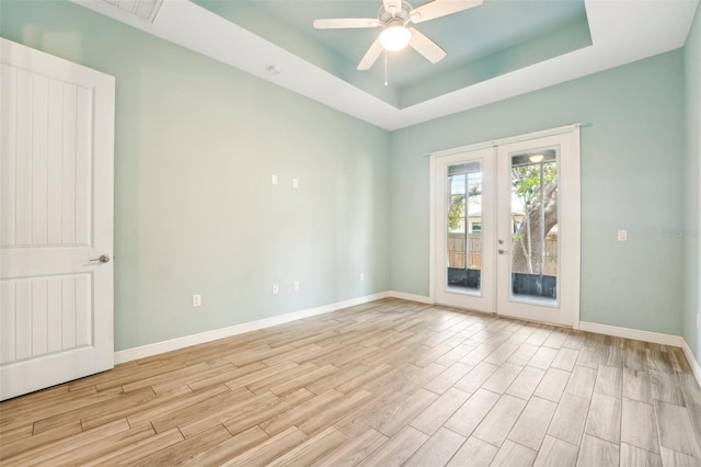 spare room with french doors, a raised ceiling, light wood-style flooring, a ceiling fan, and baseboards