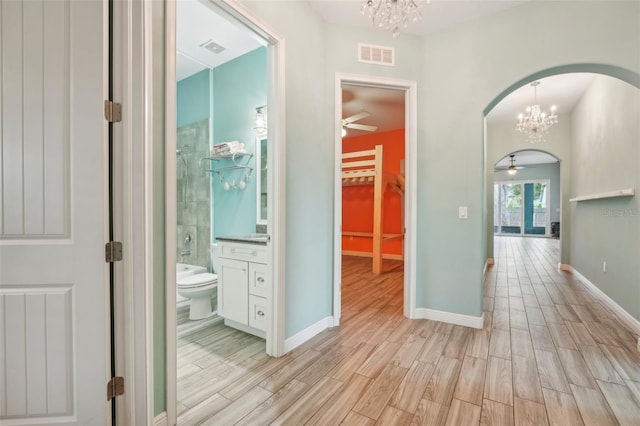 corridor featuring arched walkways, visible vents, light wood-style floors, baseboards, and an inviting chandelier