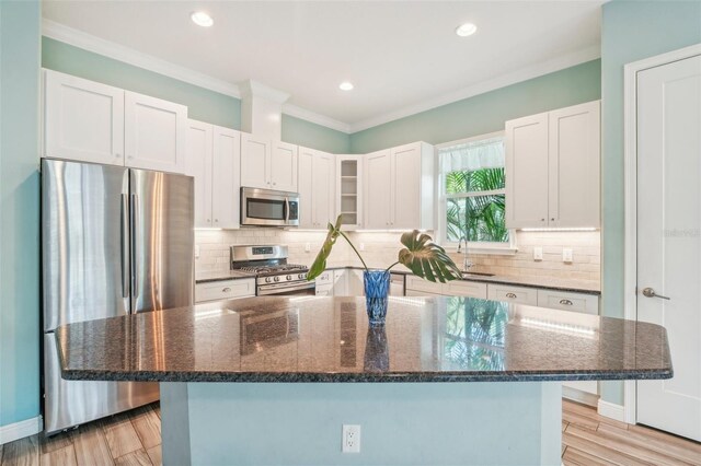 kitchen with stainless steel appliances, a sink, backsplash, a center island, and crown molding